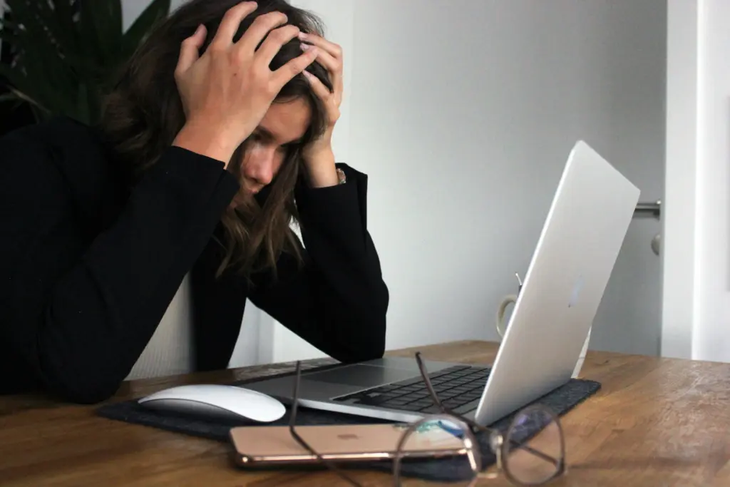 Stresszes nő laptop előtt, fejét fogva, munkahelyi kiégés és túlterheltség jelei