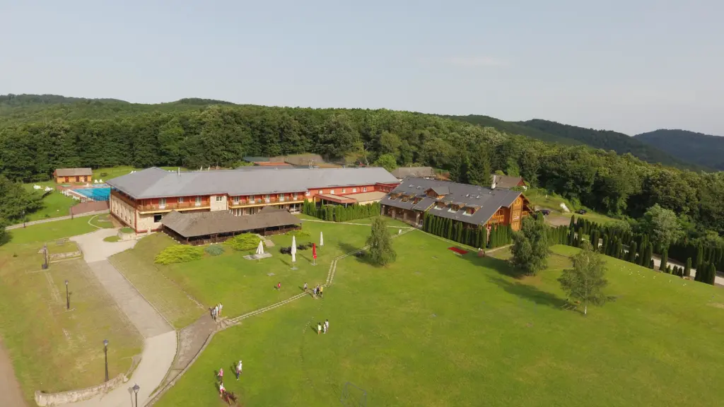 Légi felvétel a Szent Orbán Erdei Wellness Hotelről, ahol farönk épületek láthatók a Börzsöny erdős környezetében, parkosított kerttel és szabadtéri stranddal