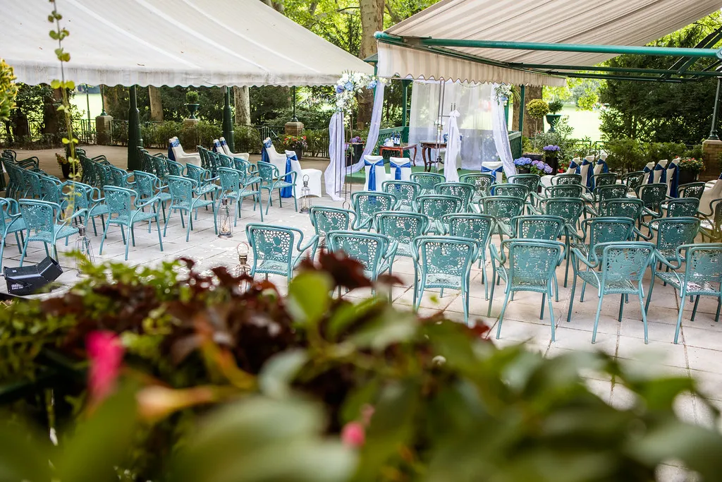 Az Ensana Grand Margitsziget teraszán esküvői helyszín berendezve, ahol türkiz székek, fehér sátor és virágdíszek láthatók platánfák lombjai alatt