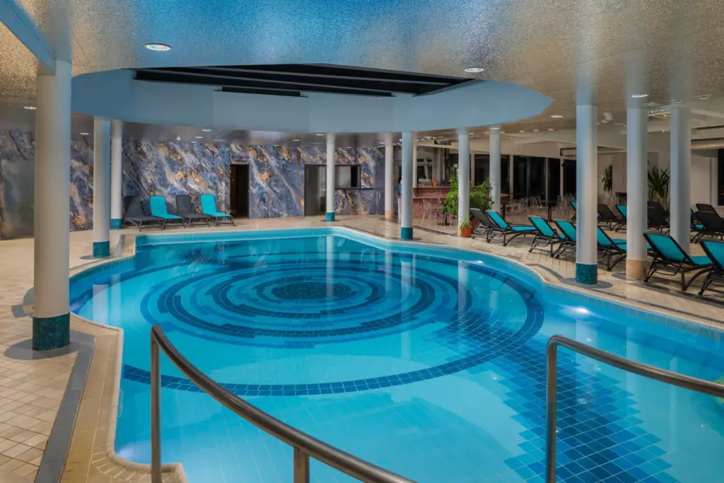 A Silvanus Hotel Visegrád beltéri wellness medencéje, ahol spirál mintázatú medencefenék és márvány falak láthatók türkiz nyugágyakkal