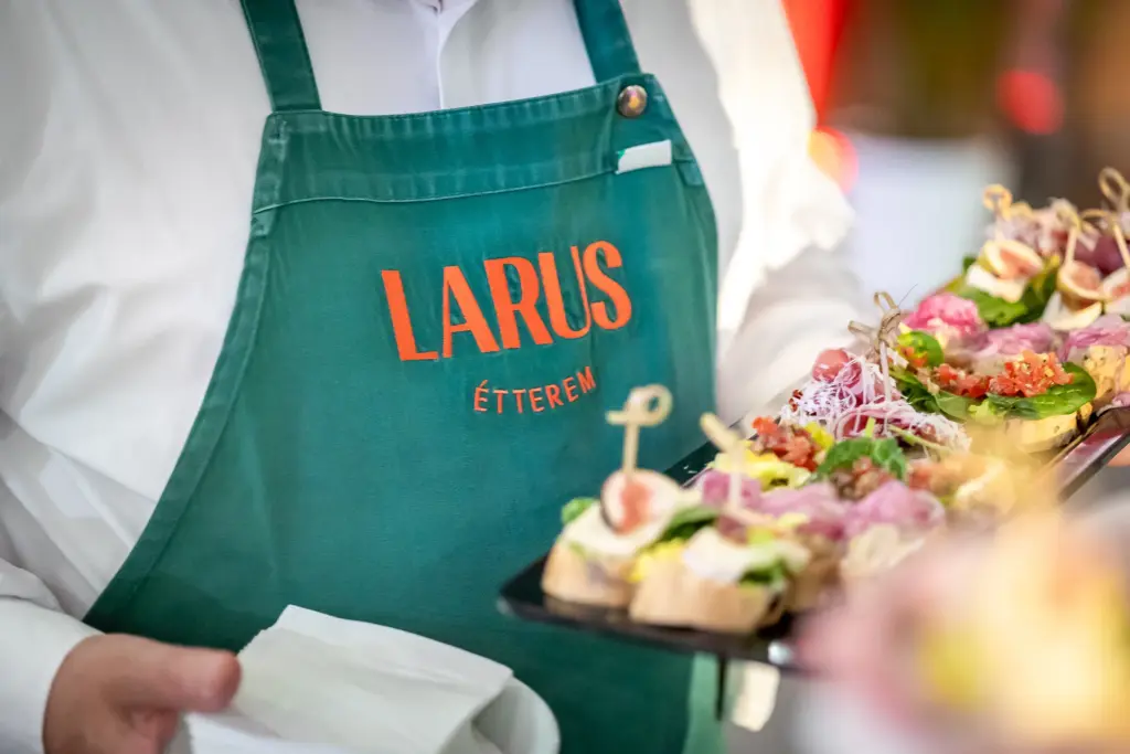 A Larus Event & Catering Budapest séfje zöld kötényben, ahol gourmet falatok láthatók tálcán színes díszítéssel