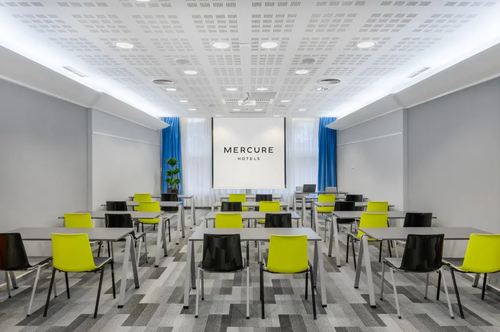A Mercure Budapest Castle Hill Szent László vagy Krisztina terme iskolapados elrendezéssel, ahol 70 fő vesz részt meetingen beépített projektorral és kék függönyökkel