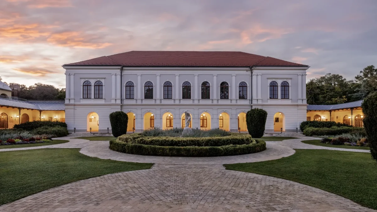 Történelmi fehér bálterem épület íves ablakokkal parkban alkonyatkor